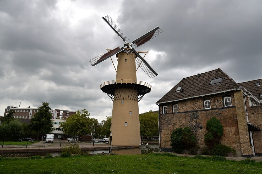 Een hoge Schiedamse molen op zijn bakstenen voet aan de rand van de stad